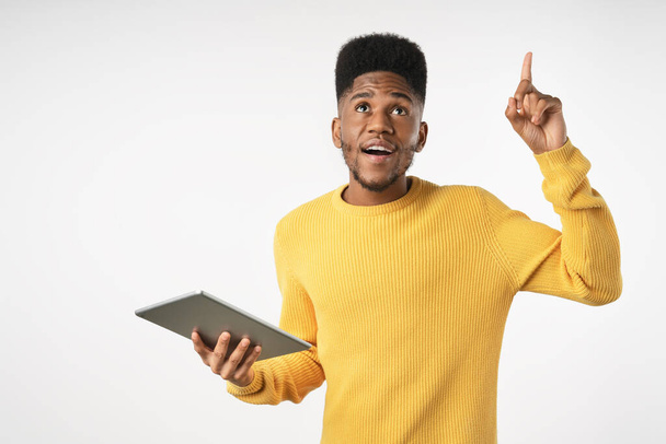 Happy excited gu holding tablet and pointing finger up standing isolated over white background - Φωτογραφία, εικόνα