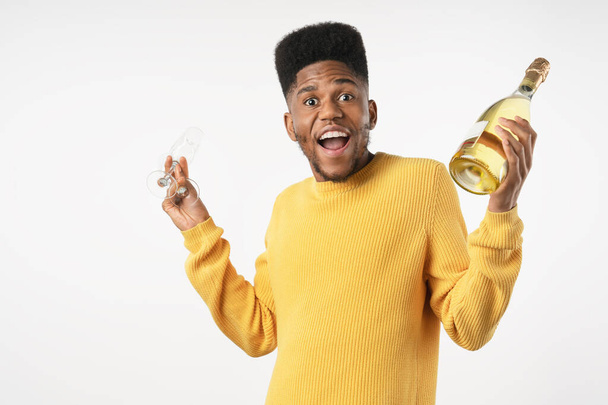 Young african man celebrating with bottle of alcohol and glasses isolated over white background - Foto, imagen