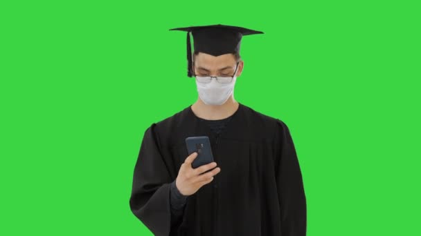 Fiatal raduate diák orvosi maszk segítségével telefon séta a zöld képernyőn, Chroma Key. - Felvétel, videó