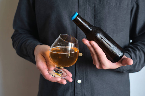 A glass of beer and bottle in the hands of a man. Tasting brewed craft beer. Lager beer with beautiful foam. Cold refreshment beverage. Alcohol drink. Relaxation and enjoyment on beer degustation - Φωτογραφία, εικόνα
