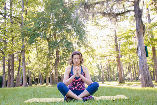 Chica sentada en la hierba en el parque y cogida de la mano en una pose de oración en el sol poniente. El concepto de un estilo de vida saludable, yoga y meditación
. - Foto, imagen