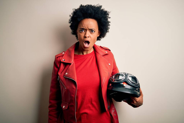 Jovem afro-americana afro motociclista com cabelo encaracolado segurando capacete de motocicleta Em face de choque, olhando cético e sarcástico, surpreso com a boca aberta
 - Foto, Imagem