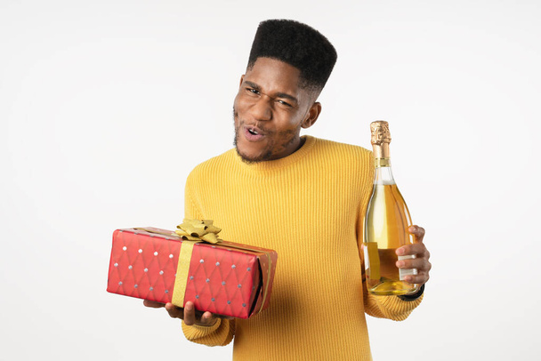 Funny young man holding present and champagne bottle isolated on white background. Celebration concept - Fotografie, Obrázek