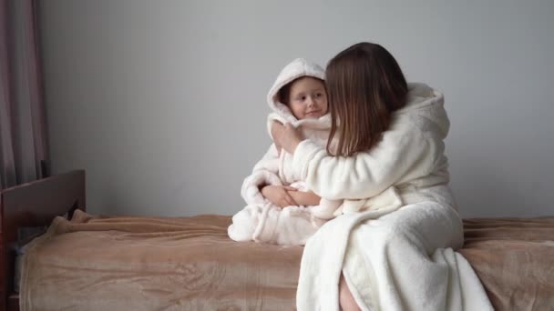 Loving cute little daughter hugging a happy young mom congratulating with mothers day concept hugging a thankful mom. Women's bathrobe. - Footage, Video