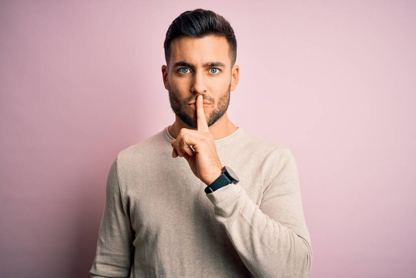 Young handsome man wearing casual sweater standing over isolated pink background asking to be quiet with finger on lips. Silence and secret concept. - Photo, Image