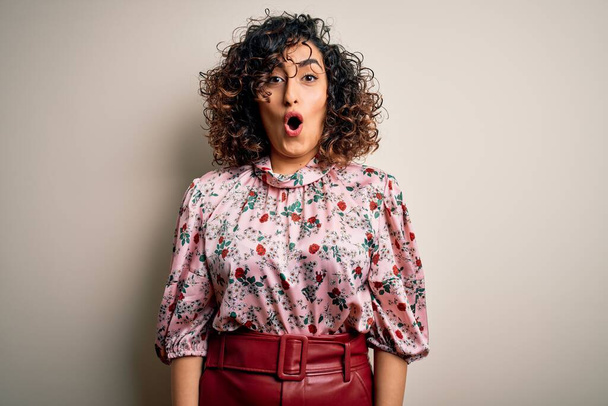 Young beautiful curly arab woman wearing floral t-shirt standing over isolated white background afraid and shocked with surprise expression, fear and excited face. - Photo, Image