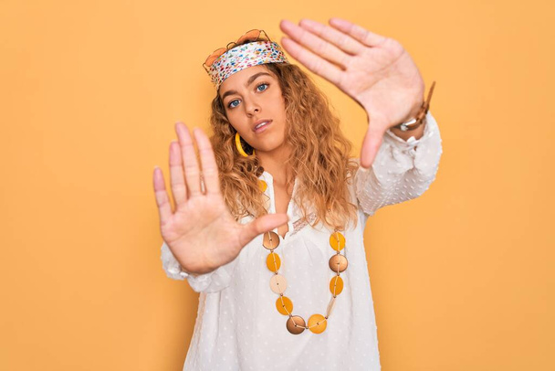 Jonge mooie blonde hippie vrouw met blauwe ogen dragen zonnebril en accessoires doen frame met behulp van handen palmen en vingers, camera perspectief - Foto, afbeelding