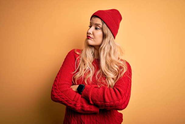 Young beautiful blonde woman wearing casual sweater and wool cap over white background looking to the side with arms crossed convinced and confident - Foto, immagini