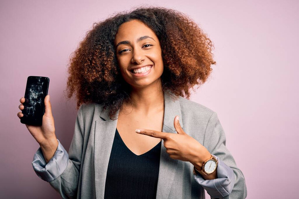 Afro saçlı, çatlak ve kırık akıllı telefon ekranı olan genç Afro-Amerikalı kadın elini ve parmağını göstererek çok mutlu görünüyor. - Fotoğraf, Görsel