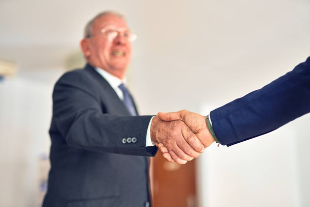 企業の労働者のグループは幸せと自信を笑顔。2人は、笑顔で合意のための握手に立っている。事務所に拍手を送るパートナー. - 写真・画像