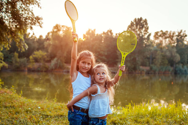 Kleine Mädchen haben Spaß im Freien, nachdem sie Badminton gespielt haben. Schwestern züchten Schläger im Frühlingspark. Aktivitäten für Kinder. Internationaler Kindertag - Foto, Bild