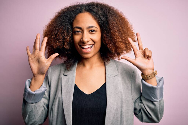 Junge afrikanisch-amerikanische Geschäftsfrau mit Afro-Haaren trägt elegante Jacke und zeigt mit Finger Nummer acht nach oben, während sie selbstbewusst und glücklich lächelt. - Foto, Bild