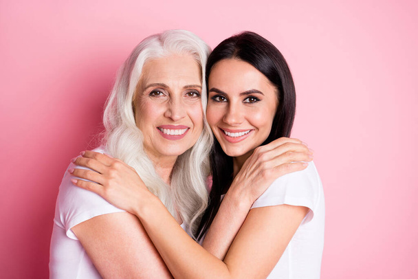 Photo of charming aged mother young pretty daughter two ladies good mood hugging best friends through years wear casual white t-shirts isolated pastel pink color background - Foto, imagen