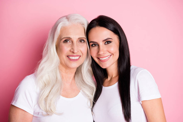 Photo of attractive old mother young pretty daughter two ladies good mood stand close best friends through years wear casual white t-shirts isolated pastel pink color background - Fotografie, Obrázek