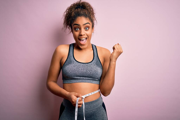 Genç Afro-Amerikan spor kızı kilo kontrolünü bel ölçüsünü kullanarak gururla bağırıyor ve zaferi ve başarıyı kutluyor. - Fotoğraf, Görsel