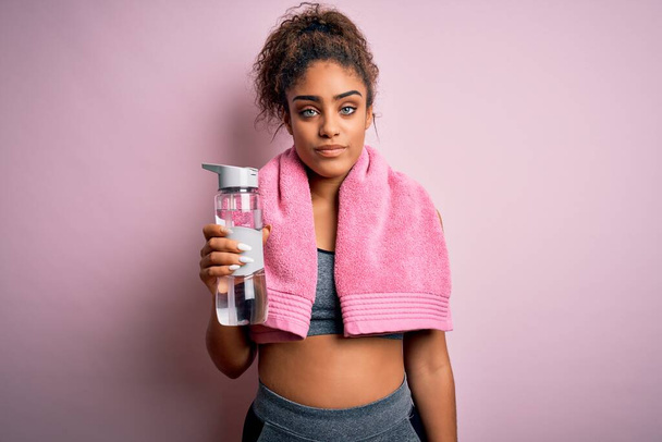 Young african american sporty girl doing sport wearing towel drinking bottle of water with a confident expression on smart face thinking serious - Photo, Image
