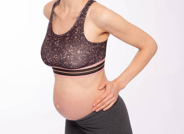 Pregnant woman has lower back discomfort; white backgrouond - Φωτογραφία, εικόνα