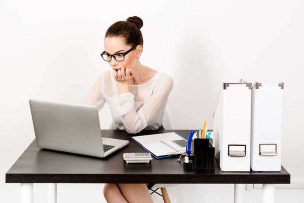 Suprised young businesswoman wearing eyewear working on laptop in white modern office. The concept of distance education or working from home in quarantine. Unemployment, the fall of stock indices, shocking news. - Valokuva, kuva