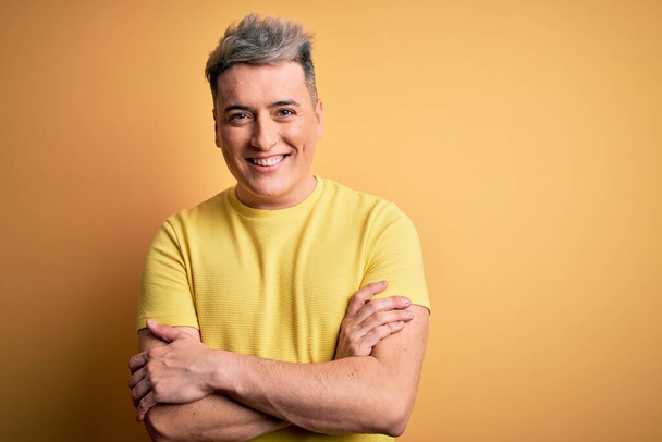Jeune homme moderne beau portant chemise jaune sur fond isolé jaune heureux visage souriant avec les bras croisés regardant la caméra. Personne positive
. - Photo, image