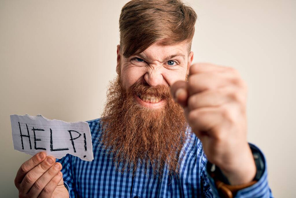 Rossa uomo irlandese con barba che tiene carta con messaggio di aiuto su sfondo blu infastidito e frustrato urlando con rabbia, pazzo e urlando con mano sollevata, concetto di rabbia
 - Foto, immagini
