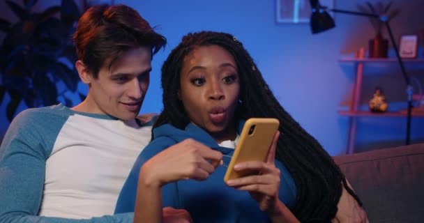 Millennial couple talking and looking at phone screen.Young woman with dreadlocks making surprised facial expression while using smartphone and spending time with boyfriend. - Séquence, vidéo