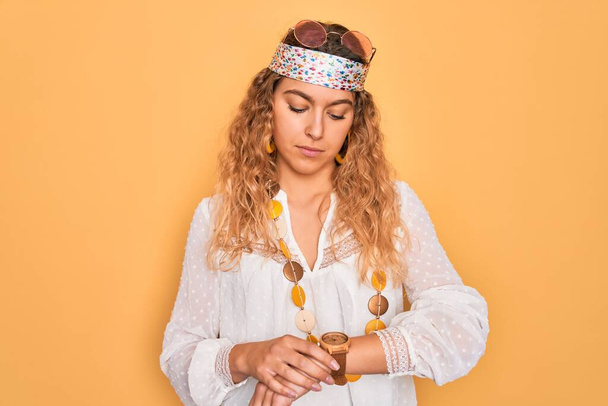 Giovane bella donna hippie bionda con gli occhi azzurri che indossa occhiali da sole e accessori Controllare il tempo su orologio da polso, rilassato e fiducioso
 - Foto, immagini