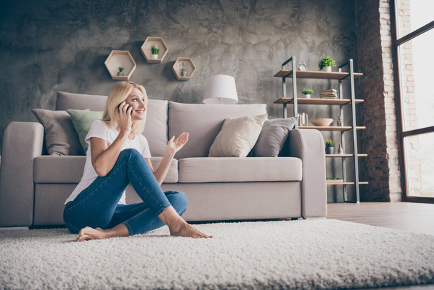 Portrait of her she nice attractive lovely pretty friendly cheerful woman sitting on carpet alone talking on phone with mom mother family in modern loft brick industrial interior style house indoors - Foto, imagen