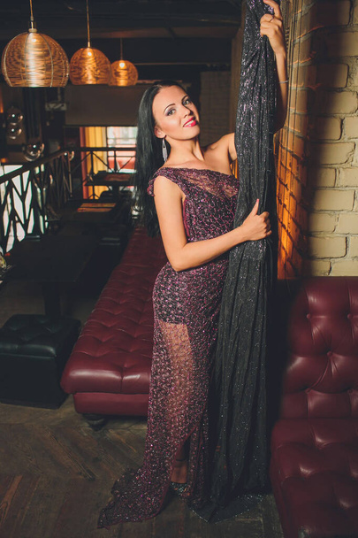 pretty woman in evening dress , with hair style posing near a restaurant bar, looking in camera. - Foto, imagen