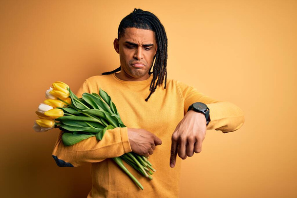 Giovane afroamericano afro romantico uomo con dreadlocks tenendo bouquet di tulipani gialli Indicando verso il basso guardando triste e sconvolto, indicando la direzione con le dita, infelice e depresso
. - Foto, immagini