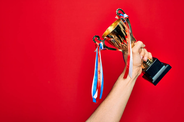 Красива рука людини тримає золоту чашку трофею над ізольованим червоним тлом
 - Фото, зображення
