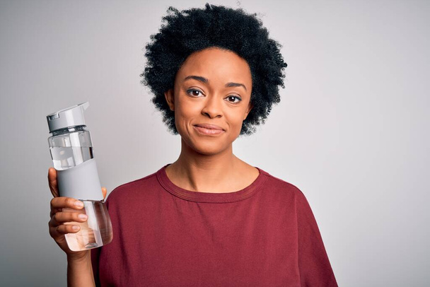 Молода афро-американська жінка з кучерявим волоссям п'є пляшку води для відсвіження з упевненим виразом розумного мислення. - Фото, зображення