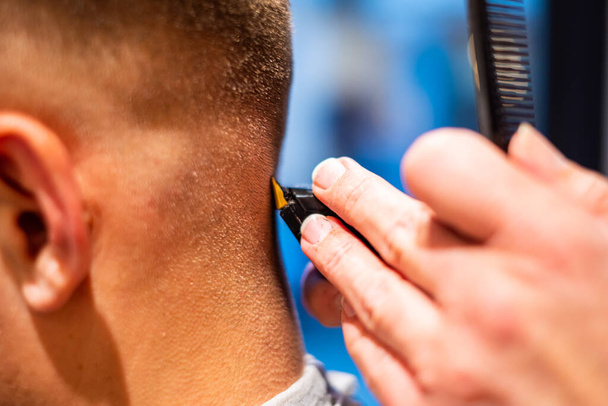Parturi leikkaa nuoren parturimiehen hiukset parturissa. lähikuva ja yksityiskohtaiset tiedot
 - Valokuva, kuva