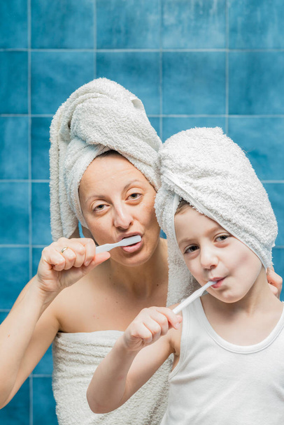 A woman and a boy with towels on their heads brushing their teeth. - Foto, Imagem