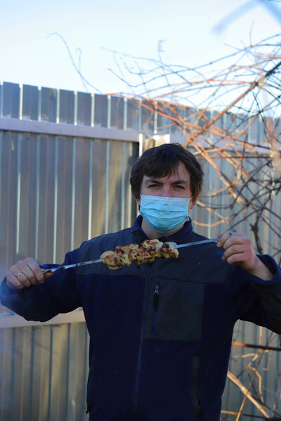 a man in a mask at the dacha roasts eats barbecue, what to do in quarantine - Foto, Imagen