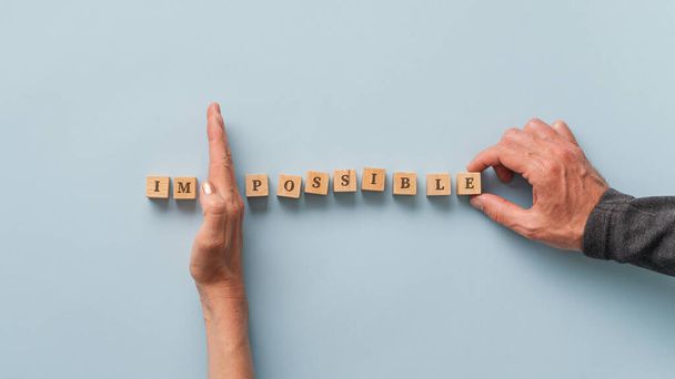 Мужские и женские руки меняют слово "невозможно" на "возможно", написанное на деревянных блоках. над синим фоном
. - Фото, изображение