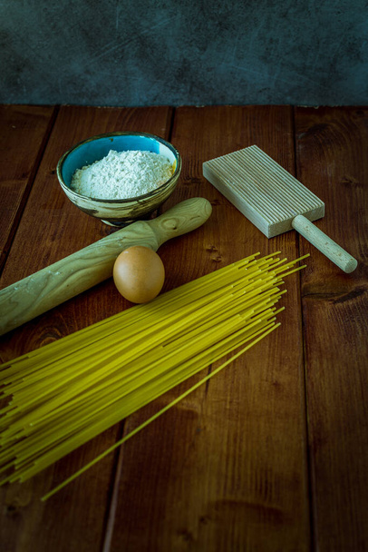 ингредиенты для приготовления домашней пасты на деревянном столе с яйцами, мукой и инструментами для выкатывания теста
 - Фото, изображение