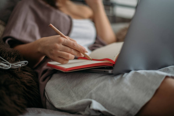 Detailní záběr rukou s tužkou, notebookem a notebookem. Mladá žena mluví po telefonu, pracuje online a píše si poznámky do zápisníku - Fotografie, Obrázek