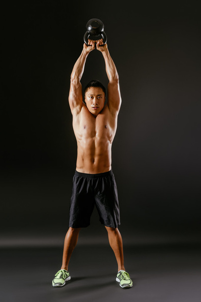 Asian man lifting a kettlebell over his head - Foto, afbeelding