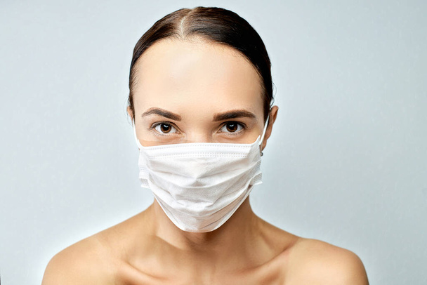 Young brunette girl with beautiful eyebrows and brown eyes looks with a grin on her face a white medical mask - Photo, image