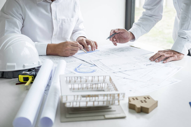 Construction engineering or architect discussing a blueprint and building model while checking information on sketching meeting for architectural project in work site. - Photo, Image