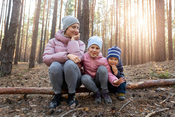 Young adult beautiful mother with two cute adorable cheerful playful caucasian children, boy and girl, having fun walking at spring or autumn forest together. Healthy outside nature family activity - Photo, Image