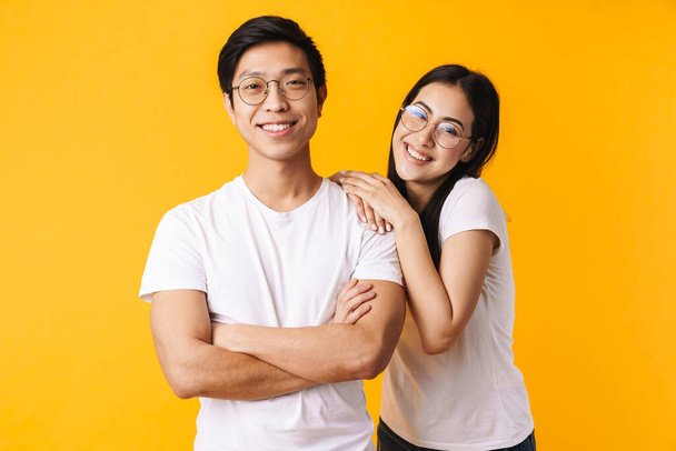 Portrait of a beautiful cheerful young asian couple wearing casual clothing standing isolated over yellow background - Photo, image