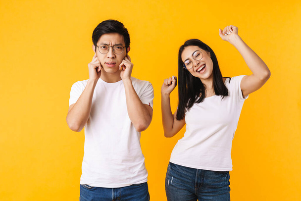 Portrait of a beautiful young asian couple wearing casual clothing standing isolated over yellow background, celebrating sucess, man is annoyed - Foto, afbeelding
