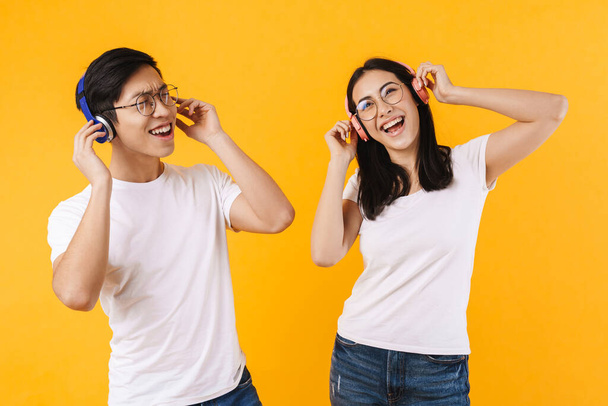 Image of joyful multinational couple in wireless headphones listening music and singing isolated over yellow background - Foto, imagen