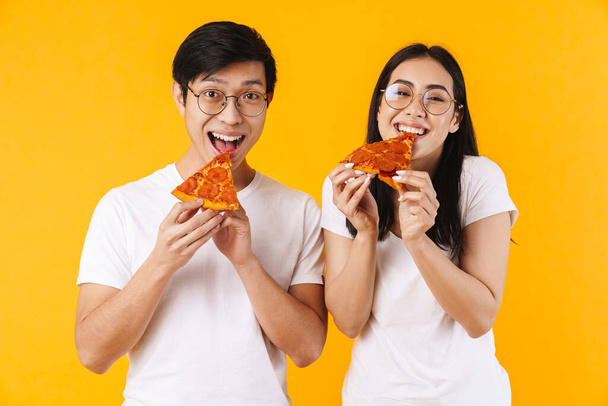 Kuva iloinen monikansallinen pari hymyilee ja syö pizzaa eristetty keltaisella taustalla
 - Valokuva, kuva