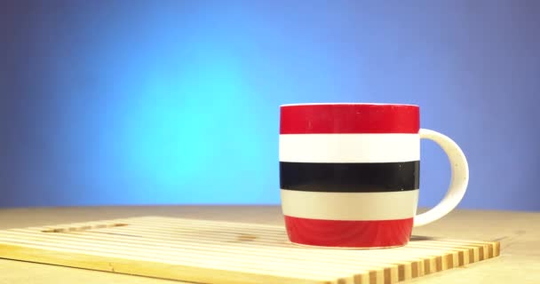 Yellow electric kettle boiling water into a cup. Hot boiled water is poured into a red, white, blue ceramic cup (mug). The blue background - Footage, Video