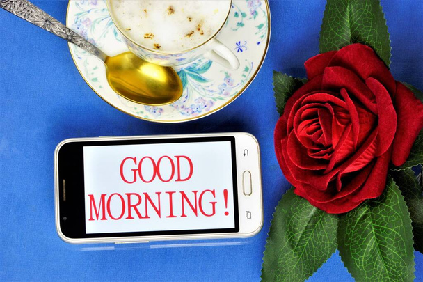 Dobré ráno-vzkaz na obrazovce smartphonu, šálek lahodné kávy pro veselost, červená růže dekorace pro radostnou náladu. - Fotografie, Obrázek