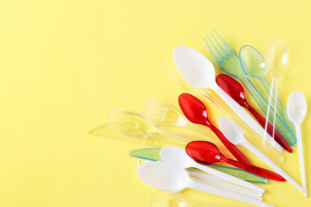 Plastic cutlery, forks, spoons and knives on yellow background. Pollution of the environment with plastic and microplastics. Copy space - Photo, Image