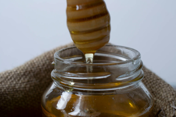 μέλι ρέει από Honey Dipper, σε ένα βάζο με μέλι. Βάζο σε σακουλάκι. υγιή έννοια της ζωής. κοντινό πλάνο - Φωτογραφία, εικόνα
