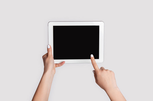 Millennial vrouw aanraken van leeg scherm van tablet apparaat op lichte achtergrond, close-up. Ruimte voor ontwerp - Foto, afbeelding